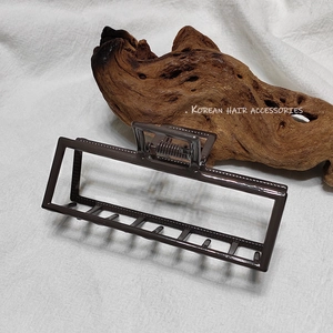 Gros plan d'une grande pince à cheveux rectangulaire marron café sur un support en bois