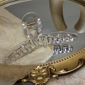 Gros plan d'une pince à cheveux transparente avec ressort doré sur miroir vintage