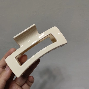 Detail of a large rectangular matte beige hair claw clip held in hand with hollow design