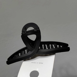 Gros plan d'une pince à cheveux noire mate au design torsadé élégant sur carte blanche