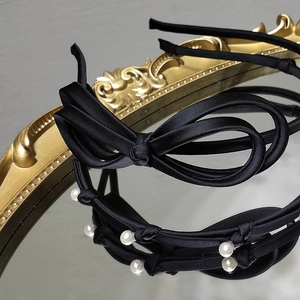 Elegant black satin headbands with chic bow and pearls displayed on vintage mirror
