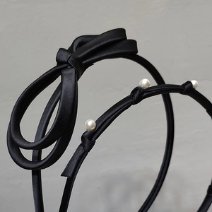 Close-up of black satin headband featuring an elegant bow and three round white pearls