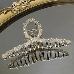 Detailed macro of golden metal hair claw clip with elegant white pearls on a mirror