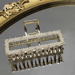 Detail of elegant gold-plated hair claw clip with pearls and hollow rectangular frame