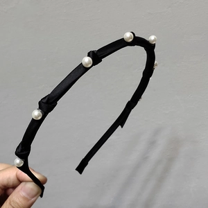 Detail view of a black thin satin headband with elegant white pearls for women