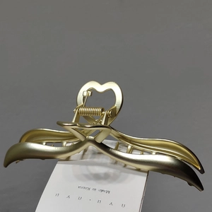 Macro detail of golden heart metal hair claw clip with matte finish and wave design