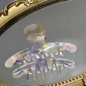 Macro shot of an iridescent translucent shark hair clip on a vintage gold mirror surface