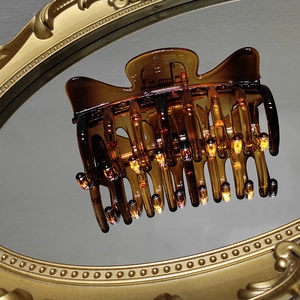 Close-up of a large amber tortoiseshell hair claw clip reflecting on a vintage gold mirror
