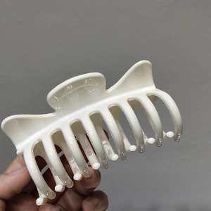 Close-up of a cream-colored cat ear hair claw clip held against a neutral wall background