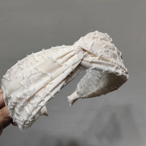 Detail of cream fabric headband featuring a unique 3D feather texture and knotted design