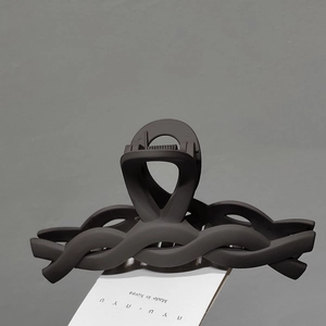 Detail of a large dark brown matte shark hair clip with a woven twist design on card