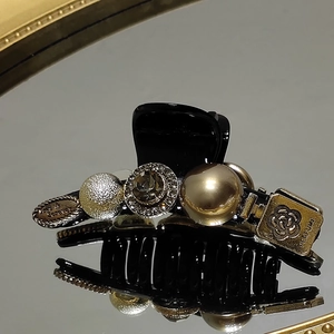 Elegant black hair claw with vintage gold charms, crystals, and pearl accents in mirror reflection