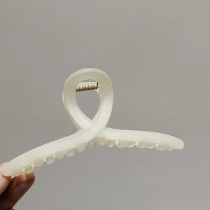 Gros plan d'une pince à cheveux mate crème de grande taille au design torsadé minimaliste