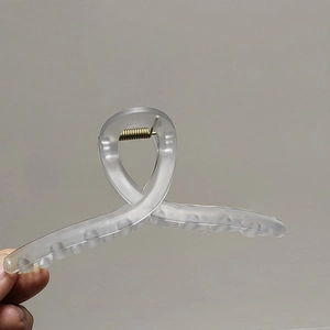 Détail d'une grande pince à cheveux transparente mate avec design croisé et ressort doré