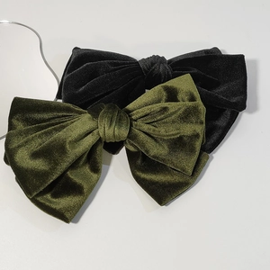 Detail of large velvet bow hair clips in black and olive green on a white surface