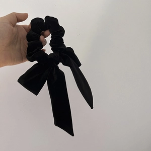Detail of elegant black velvet hair scrunchie with long ribbon bow held in hand