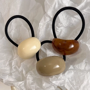 Macro detail of three minimalist resin hair ties in cream, amber, and khaki colors