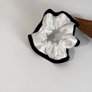 Détail macro du chouchou en satin blanc avec liseré noir contrasté au style français