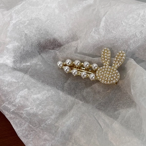 Détail d'une barrette à cheveux en perles dorées avec motif lapin sur papier blanc froissé