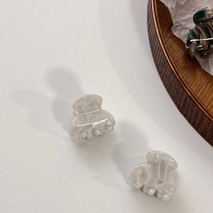 Detail of small acetate hair claw clips with elegant cream marble texture on a white background