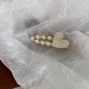 Détail d'une pince à cheveux en cœur dorée avec perles blanches sur papier plissé