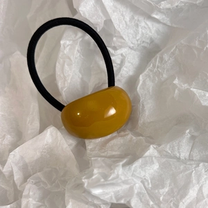 Detail of amber resin bead on black high-elastic hair tie over textured white paper