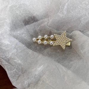 Détail de la pince à cheveux dorée ornée de perles blanches et d'un design en étoile