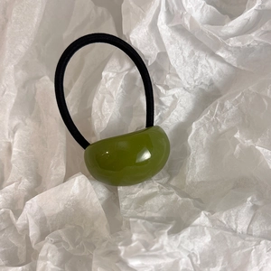 Detail shot of a glossy olive green bean-shaped charm on a black elastic hair tie