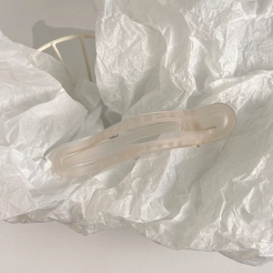 Close-up of a matte cream hair claw clip placed on textured white wrinkled paper