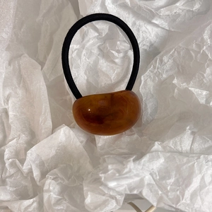 Close-up of a minimalist amber resin oval bead on a black elastic hair tie for women