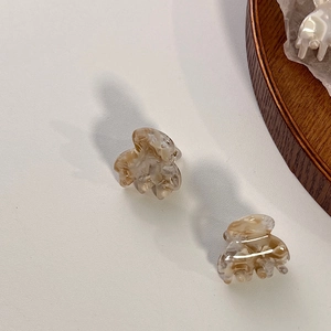 Detail view of small marble pattern acetate hair claws on a wooden tray surface