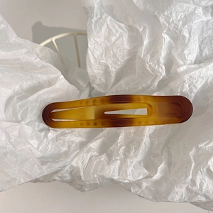 Macro view of a matte amber tortoiseshell hair claw clip on white textured paper
