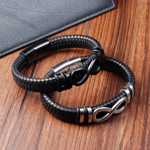 Dettaglio di bracciali in pelle nera intrecciata con simbolo infinito su legno