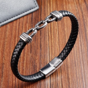 Detailansicht eines schwarzen Lederarmbands mit silbernen Metallringen auf Holzgrund