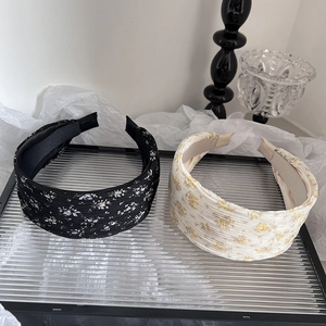 Détail de serre-têtes larges à fleurs noir et beige sur un plateau de verre chic