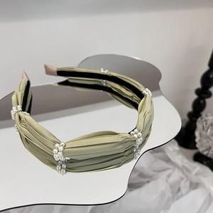 Elegant sage green fabric headband with white pearl clusters on a wavy mirror surface