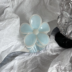 Close-up of a translucent light blue flower hair claw clip on a stylish mirror surface