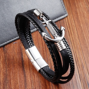 Close-up of black braided leather bracelet featuring a silver metal anchor pendant on wood
