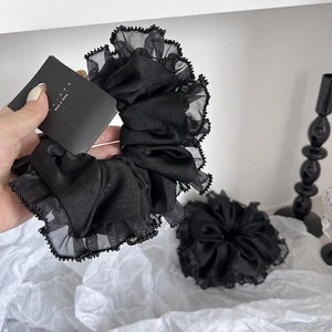 Détail d'un chouchou en tulle plissé noir avec bordure en perles sur tissu blanc vintage