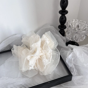 Detail of cream oversized lace scrunchie with faux pearls on a silver display tray