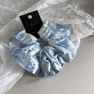 Details des blauen Seiden-Scrunchies mit Blumenstickerei auf einer Markenkarte