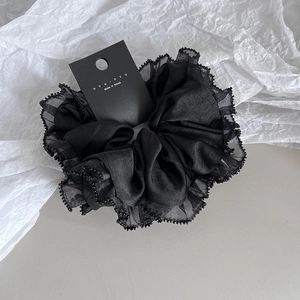 Chouchou noir en satin avec bord en mesh et perles sur fond de papier froissé blanc