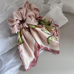 Detail of pink floral silk scrunchie with long ribbons on white textured paper