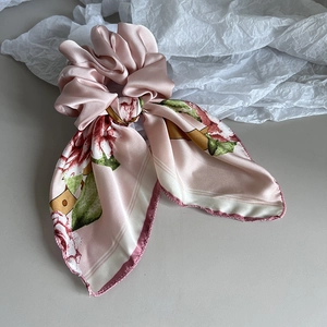 Close-up of pink satin floral bow scrunchie with elegant long ribbons on white paper