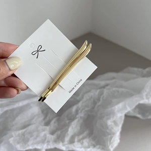 Close-up of minimalist gold metal hair clips on white card over textured fabric