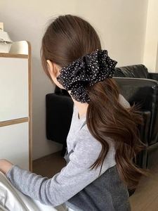 Detail of oversized black polka dot sheer fabric scrunchie worn on a low ponytail