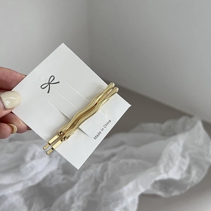 Close-up of two wavy golden alloy hair clips displayed on a branded white card