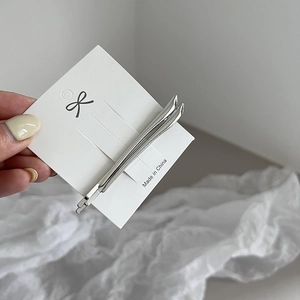 Close-up of two polished silver minimalist hair clips on a white presentation card