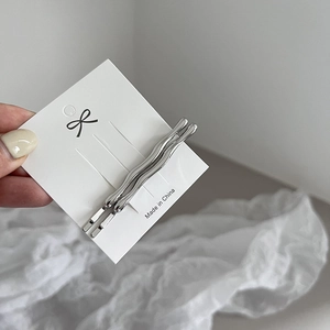Detail showing two silver wave-shaped metal hairpins on a minimalist display card