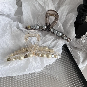 Elegant pearl bow hair claw clip set with rhinestone accents on a glass surface